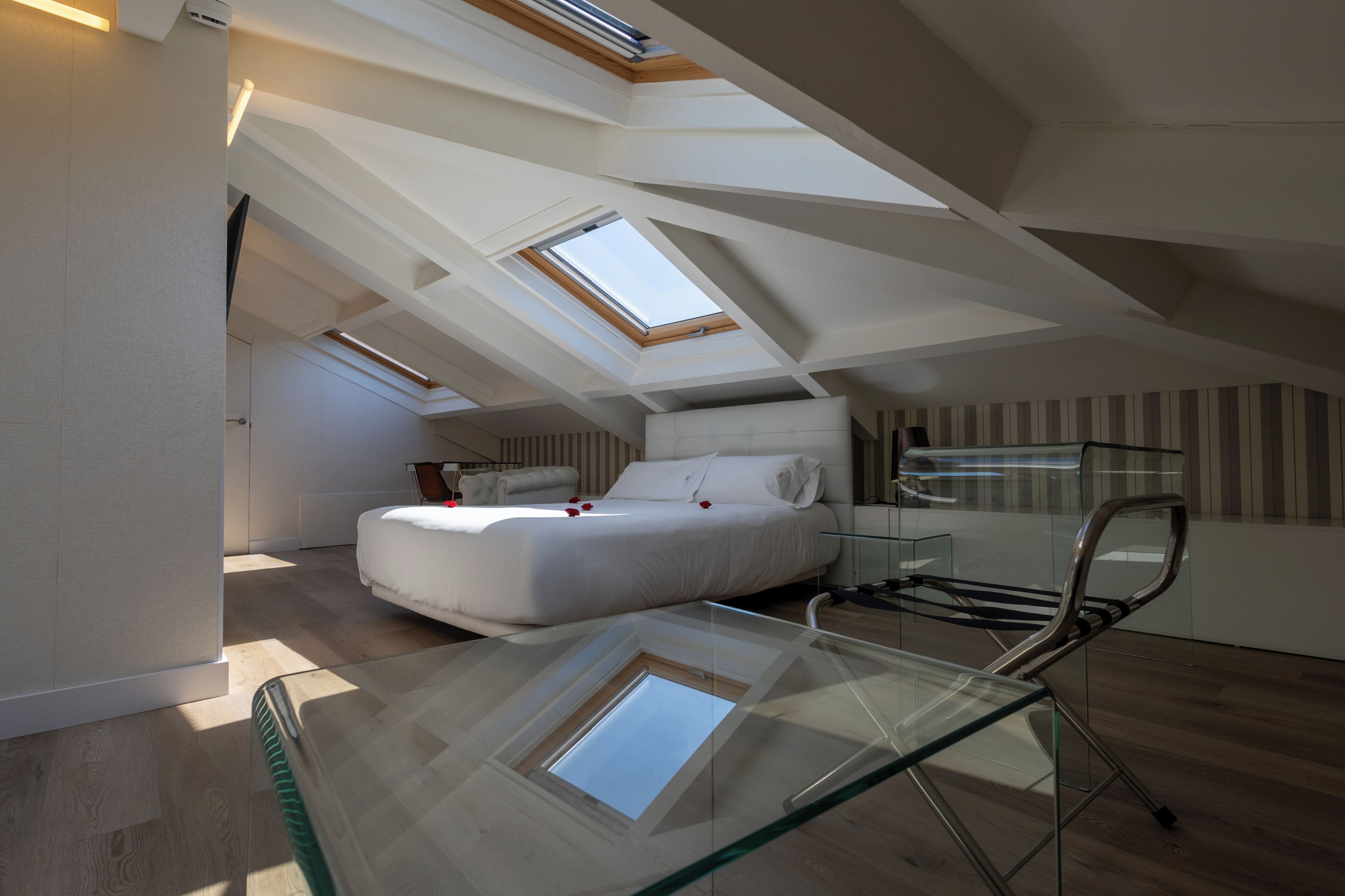 Ein Schlafzimmer im Dachgeschoss mit einem Glastisch, einem Bett und Dachfenstern.