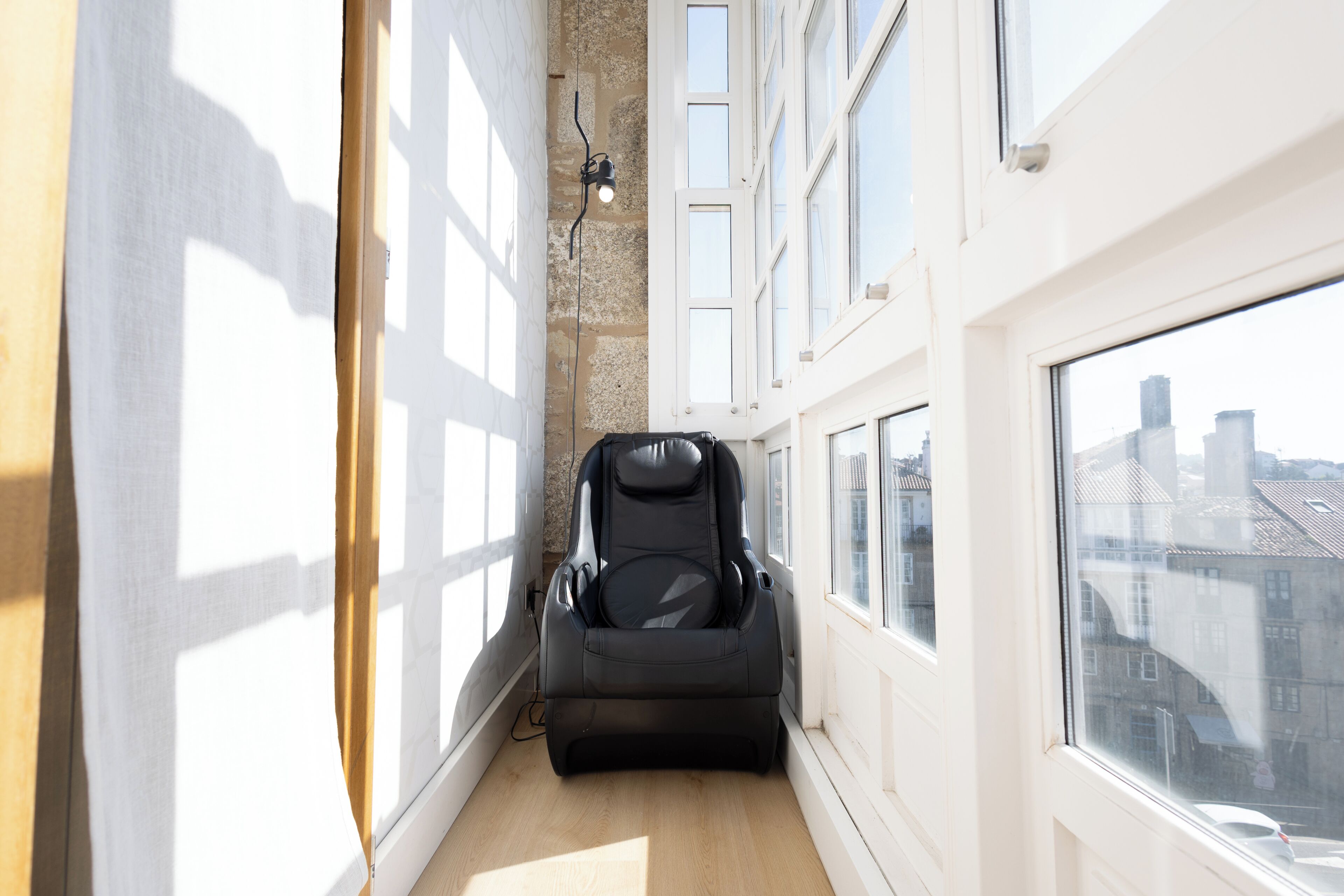 A narrow corridor with a massage chair, large windows, and a city view.