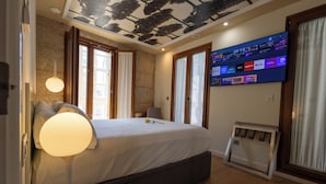 Ein Schlafzimmer mit Bett, Nachttischlampe, Fernseher und Blick ins Freie.