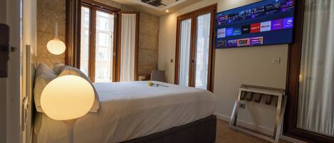 A bedroom with a bed, bedside lamp, TV, and a view of the outside.