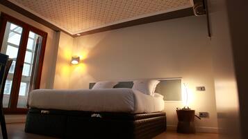 A bedroom with a bed, a nightstand, a wall-mounted lamp, and a window with curtains.