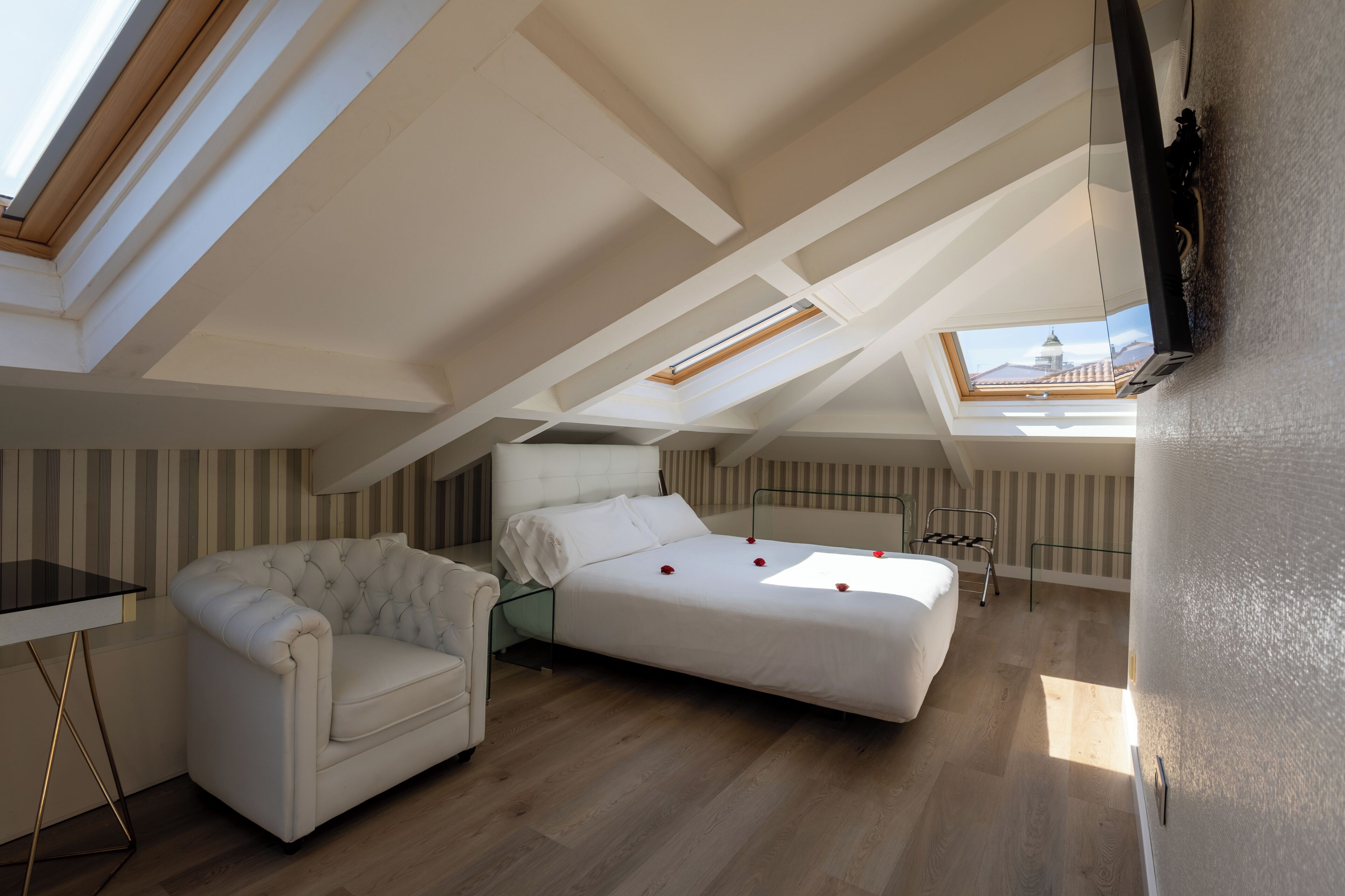 A loft bedroom with a bed, a sofa, a TV, and a skylight.