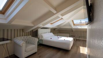 A loft bedroom with a bed, a sofa, a TV, and a skylight.