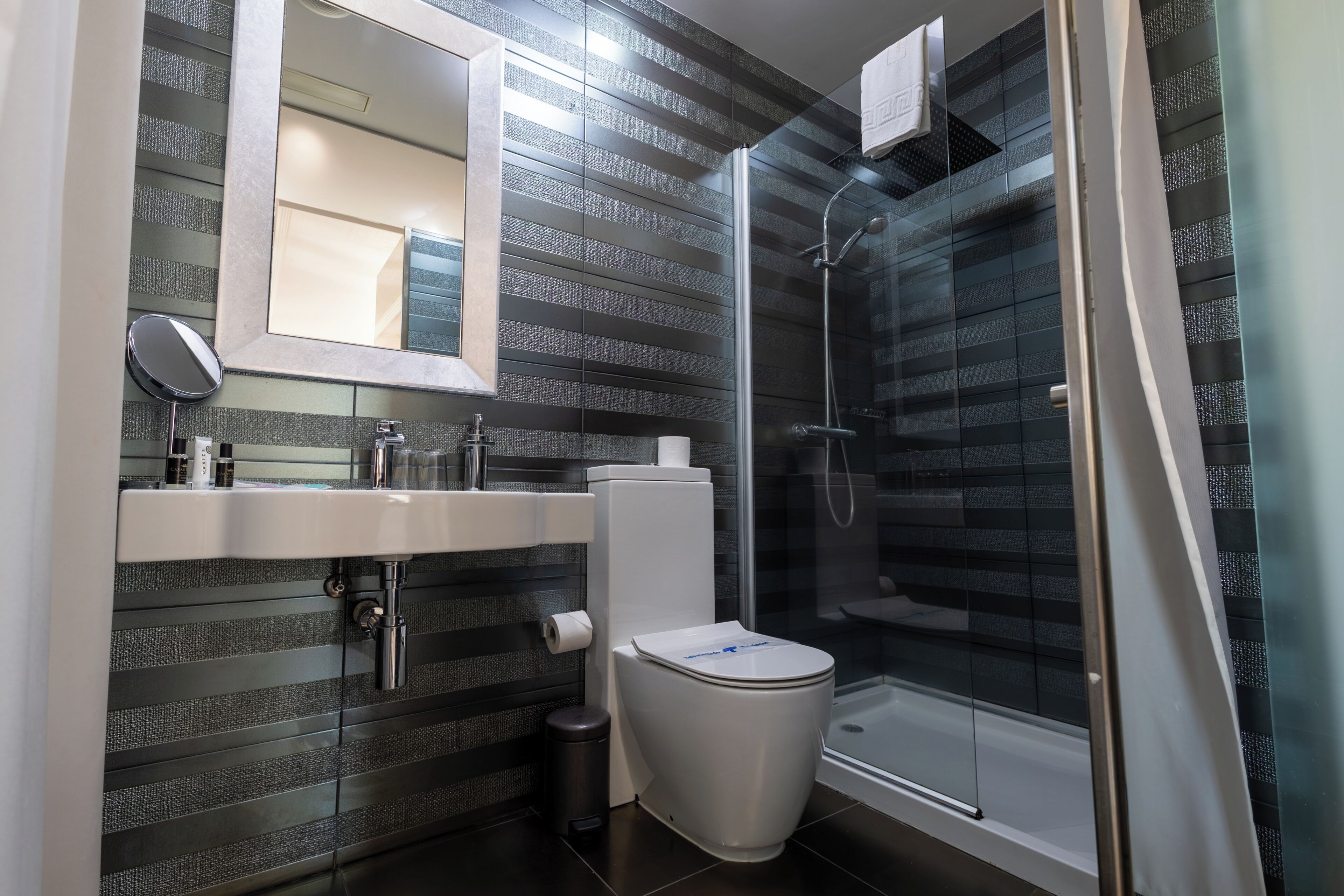 A modern bathroom with a glass shower enclosure, a white toilet, and a sink with a mirror above it.
