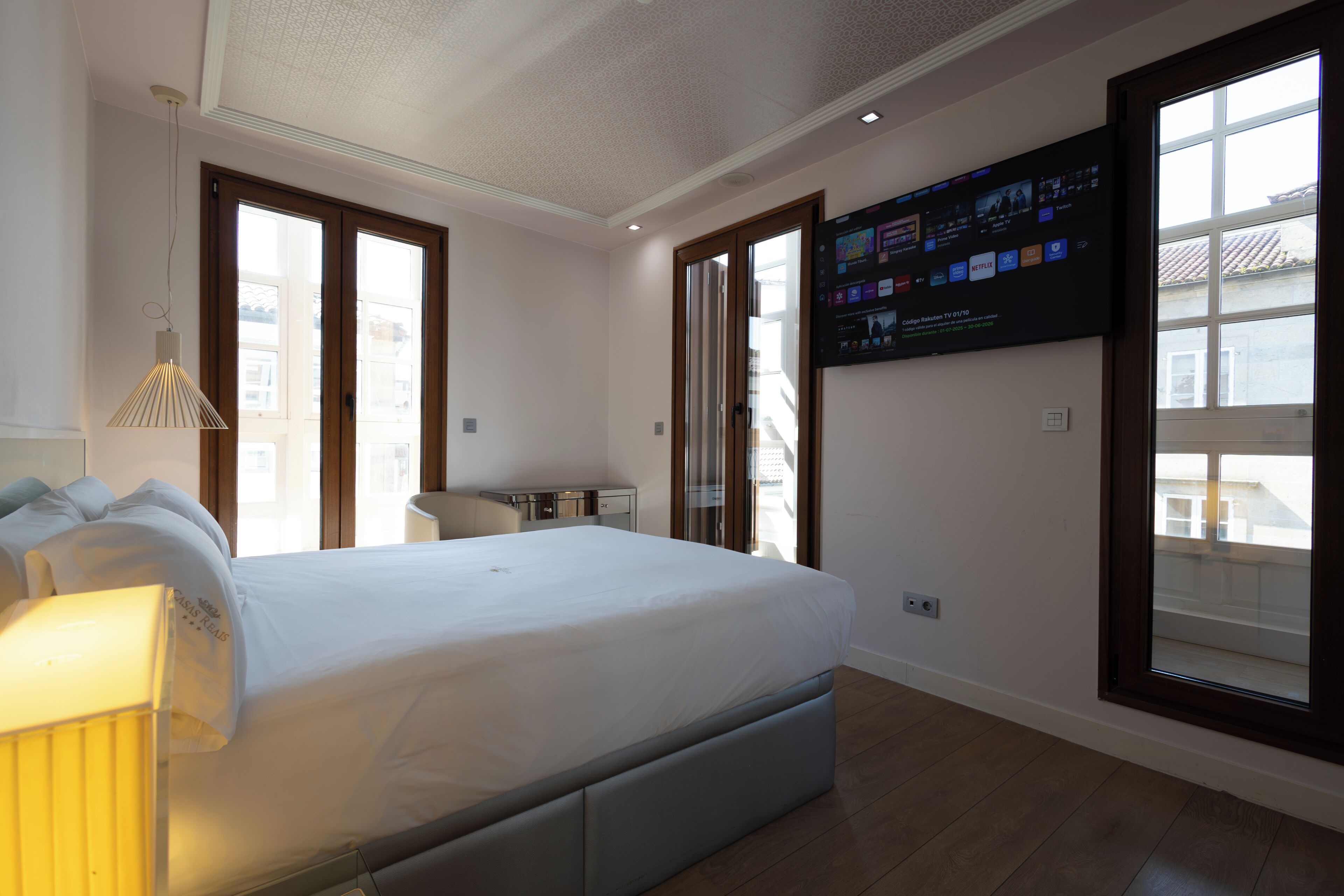 A bedroom with a bed, a desk, a chair, a TV mounted on the wall, and a window.