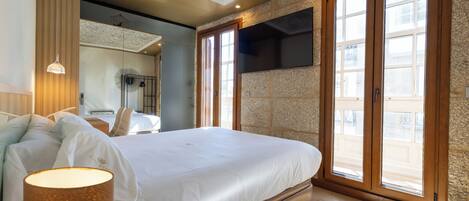 A bedroom with a large bed, a TV mounted on the wall, and a balcony with large windows.
