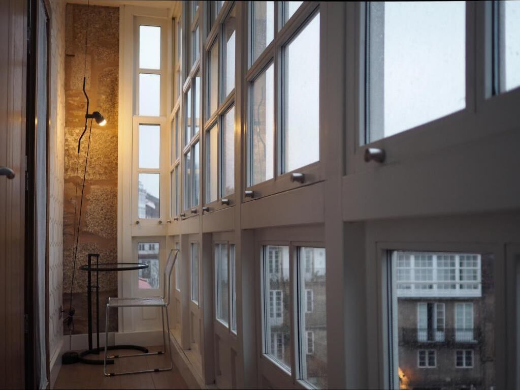 Un couloir avec de grandes fenêtres, une chaise en métal et un lampadaire.