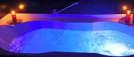 A hot tub with a handle, two candles, and a dark tiled wall.