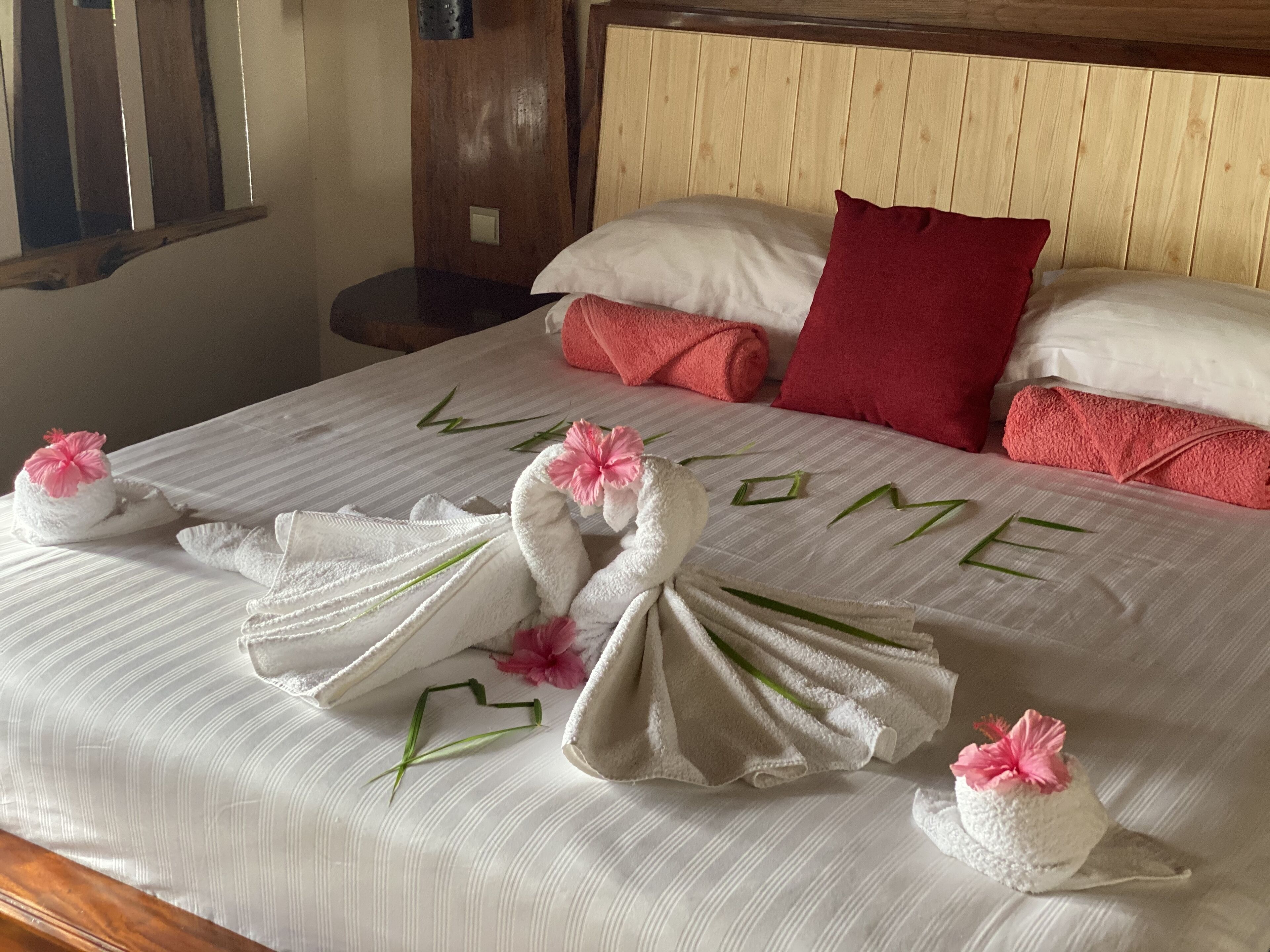 A neatly made bed with towels and flowers arranged to spell "WELCOME" on the bedspread.