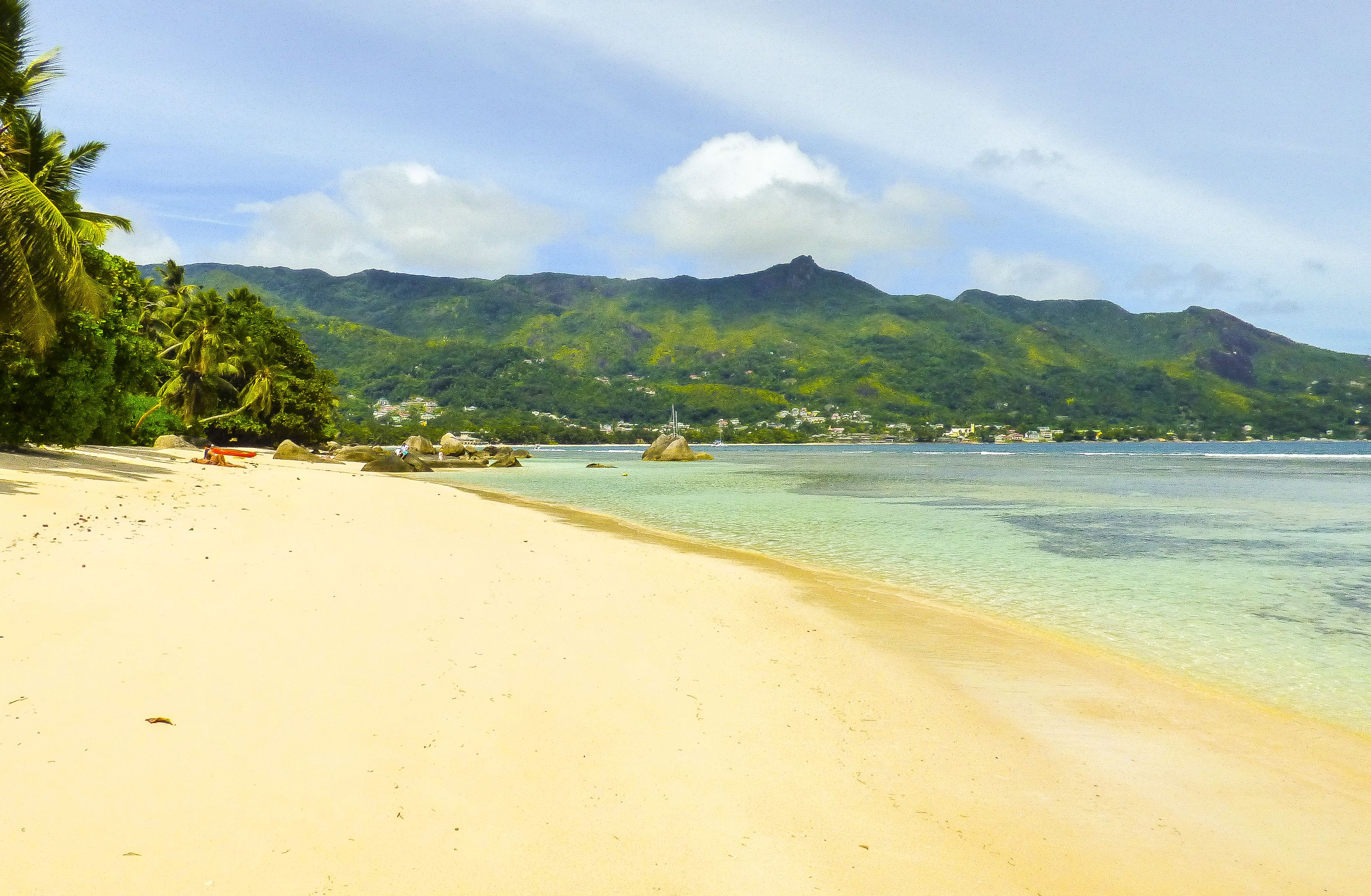 Uma praia com águas turquesa cristalinas, areal arenoso e montanhas verdejantes ao fundo.