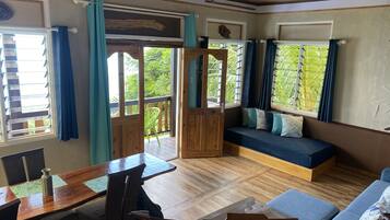 Una habitación con una mesa de madera, sillas, un banco con cojines y vistas a zonas verdes a través de ventanas amplias.