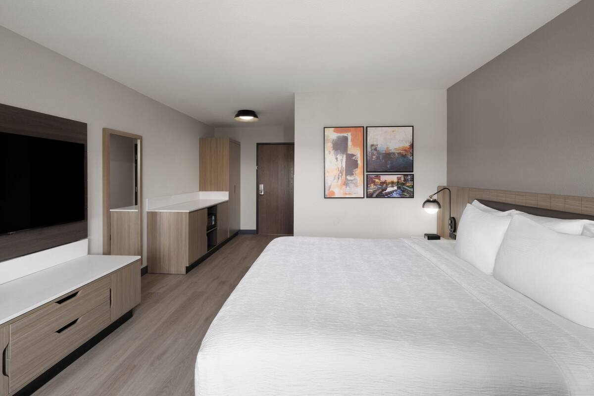 Una habitación de hotel moderna con una cama grande, un televisor de pantalla plana, un escritorio y un armario.