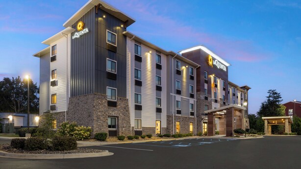 A multi-story hotel with a modern design, featuring a prominent 'La Quinta' sign, a parking lot, and a landscaped entrance area.