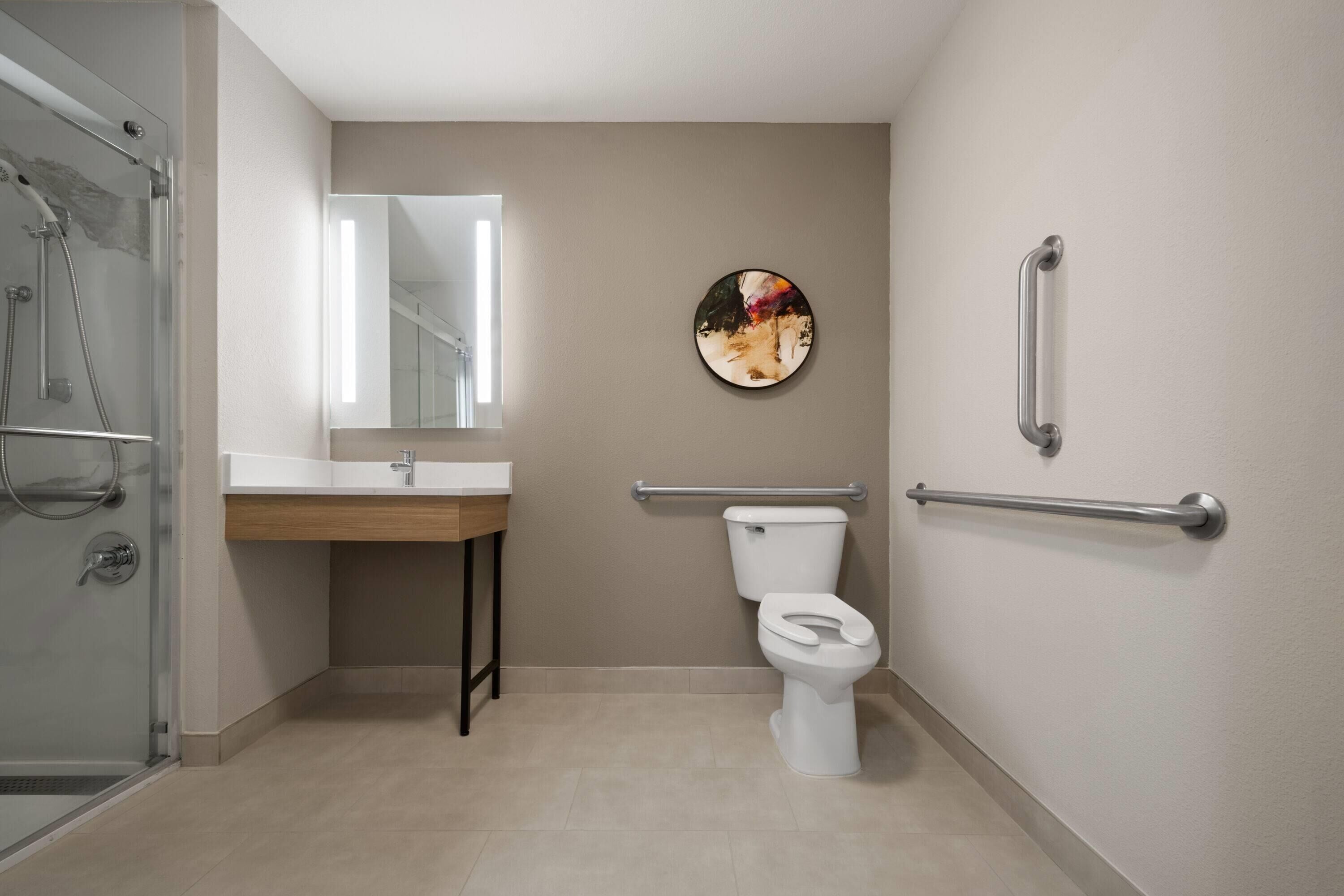 Un baño moderno con cabina de ducha de vidrio, un lavabo blanco, un inodoro y un pasamanos en la pared.