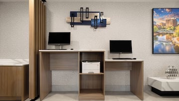 A modern office space with two desks, each with a computer monitor and a printer. There is a decorative wall piece above the desks and a framed picture on the wall to the right.