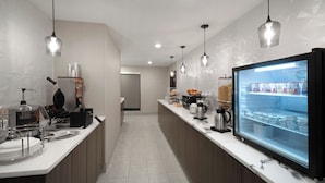 A modern kitchen with a refrigerator, coffee machine, and various food items.