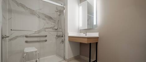 Un baño moderno con cabina de ducha de vidrio, un lavabo blanco y un mueble de tocador de madera.