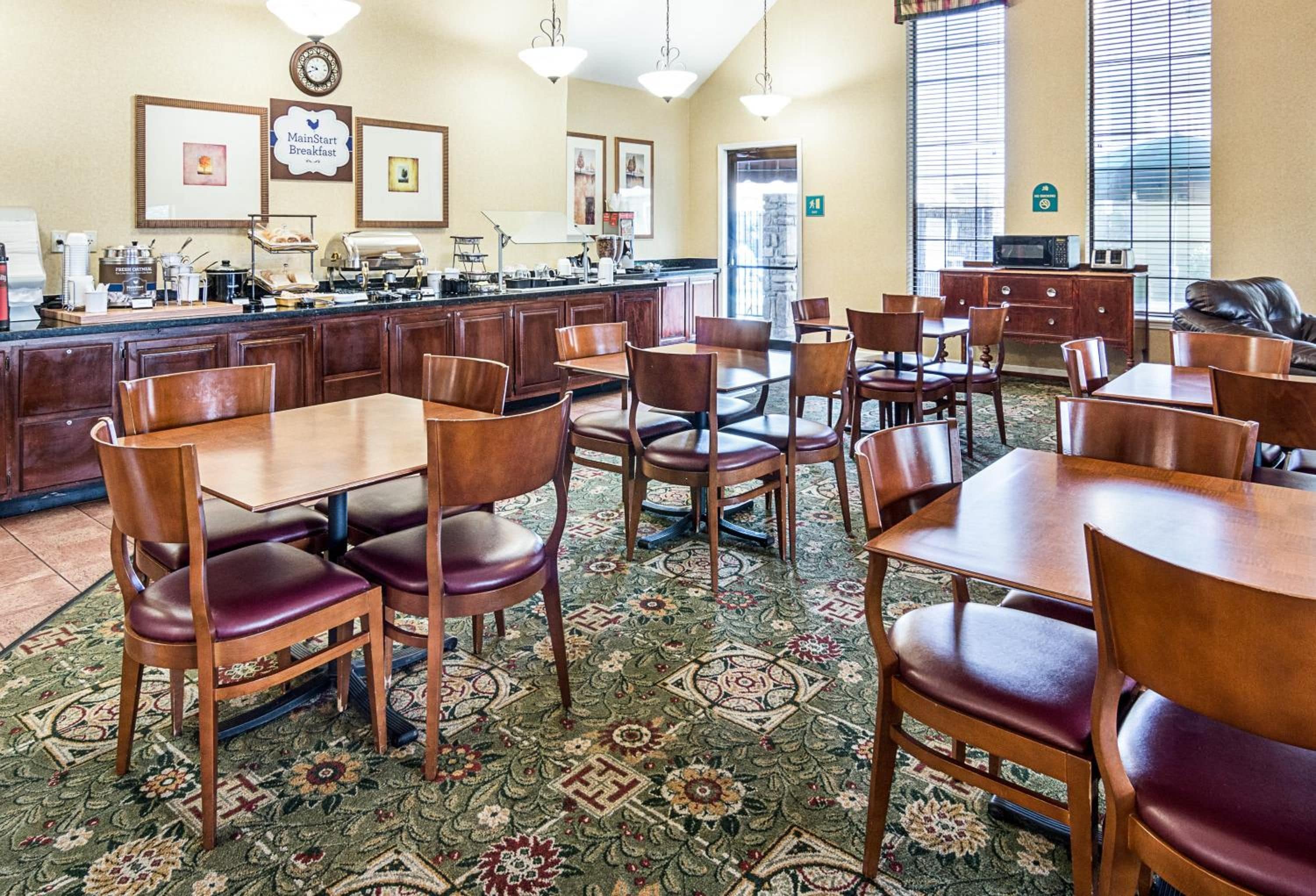 A restaurant with wooden tables and chairs, a kitchen area, and a patterned carpet.
