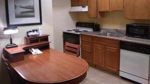 A compact kitchen with wooden cabinets, a stove, a microwave, and a sink. - Extended Studio Suite Hotel (Bossier City)