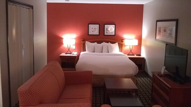A hotel room with a bed, two bedside tables with lamps, a sofa, a TV, and a wardrobe. - Extended Studio Suite Hotel (Bossier City)