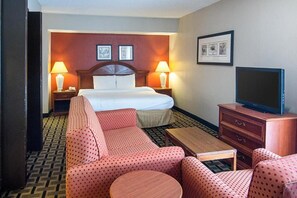 A hotel room with a bed, two bedside lamps, a television, a sofa, a coffee table, and a patterned carpet. - Extended Studio Suite Hotel (Bossier City)