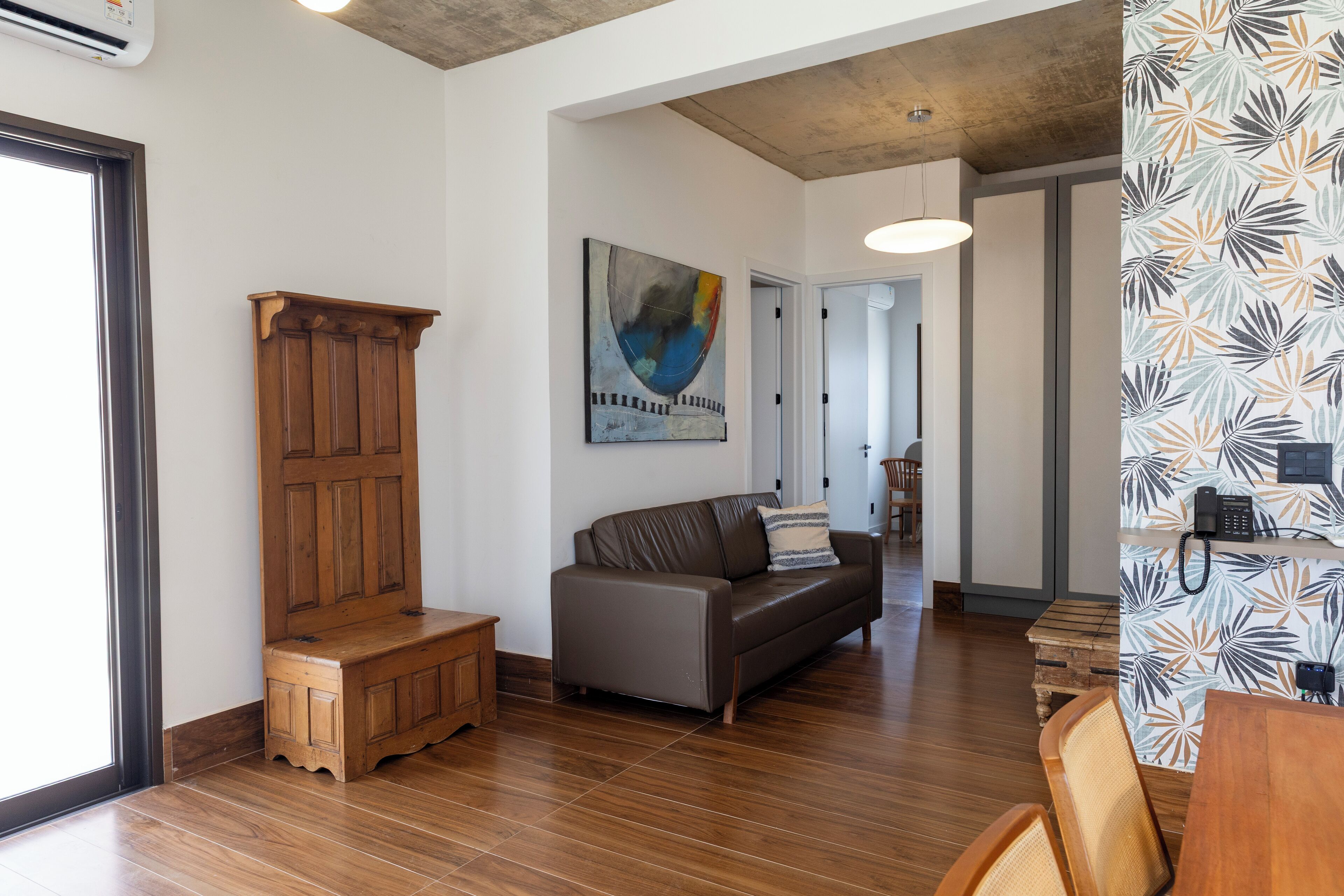 A modern living room with a wooden bench, a leather sofa, and a dining area with a wooden table and chairs.