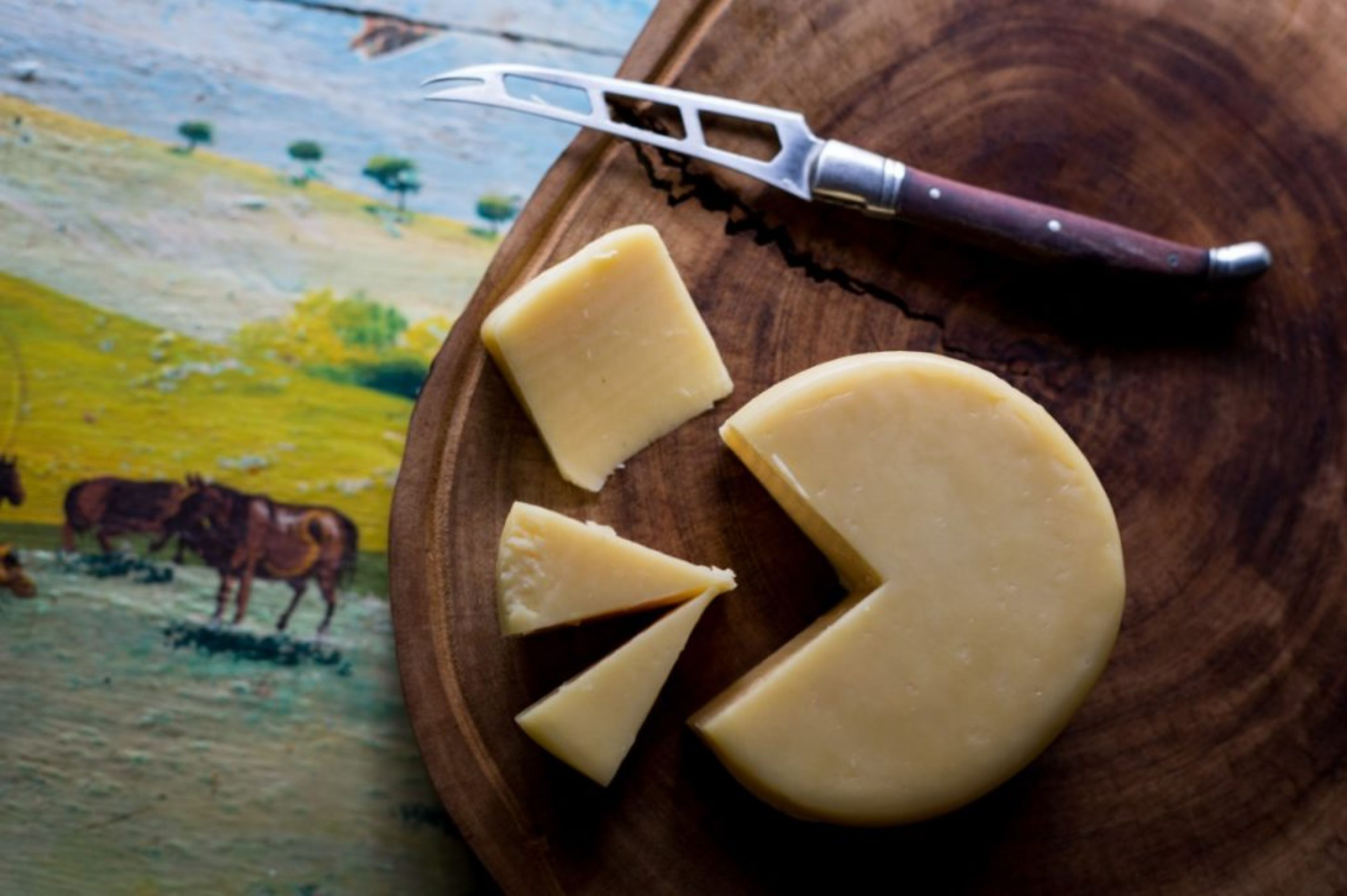 A wooden board with cheese and a cheese knife.