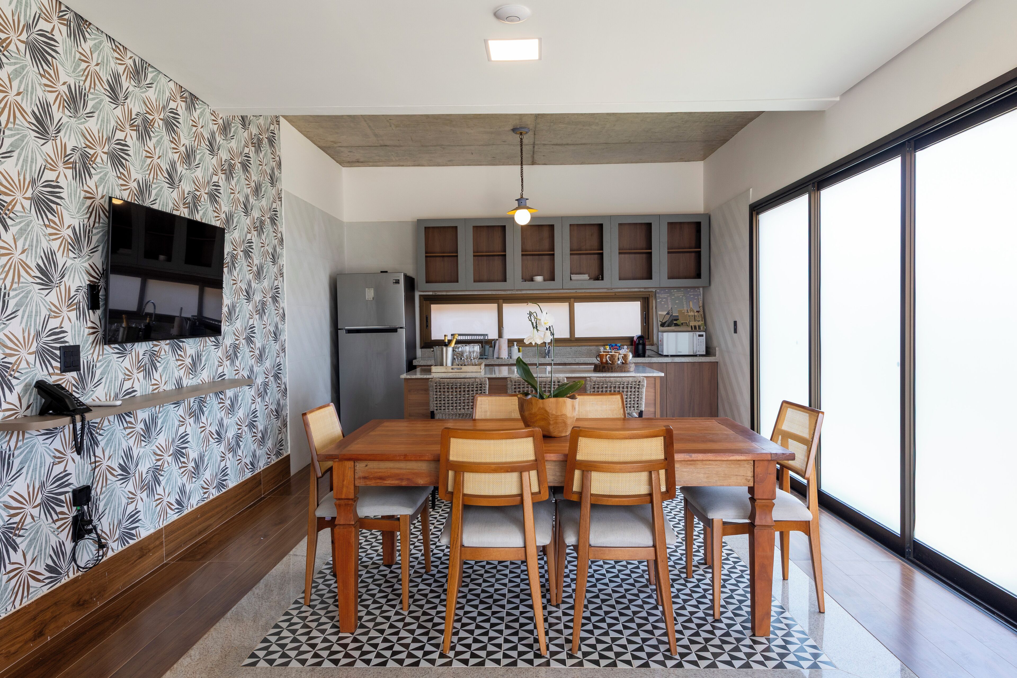Cozinha moderna com área de refeições, com uma janela ampla, televisão de tela plana e painel de fundo estampado.
