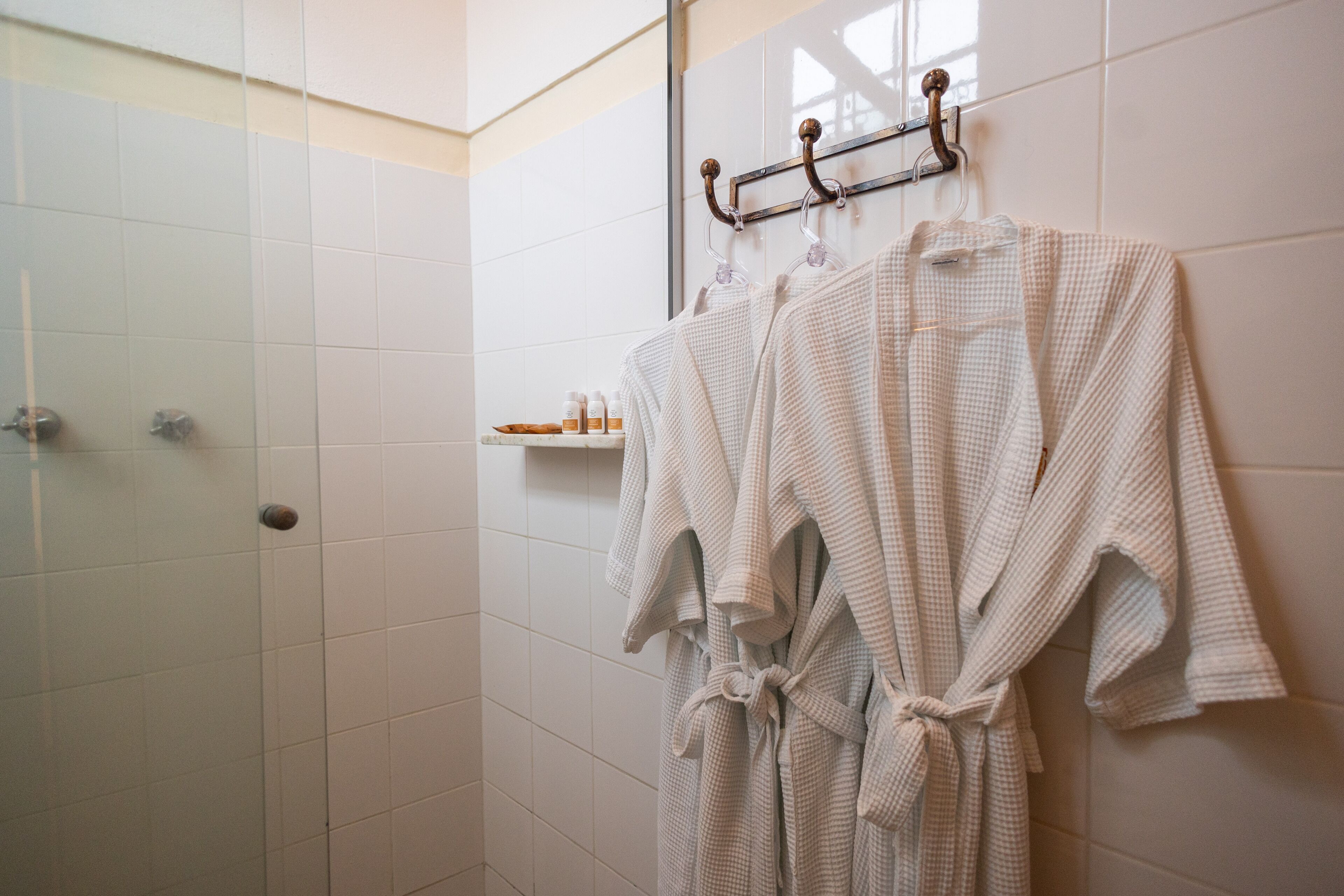 A bathroom with white tiled walls, a shower area, and a towel rack with two towels.