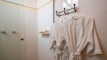 A bathroom with white tiled walls, a shower area, and a towel rack with two towels.