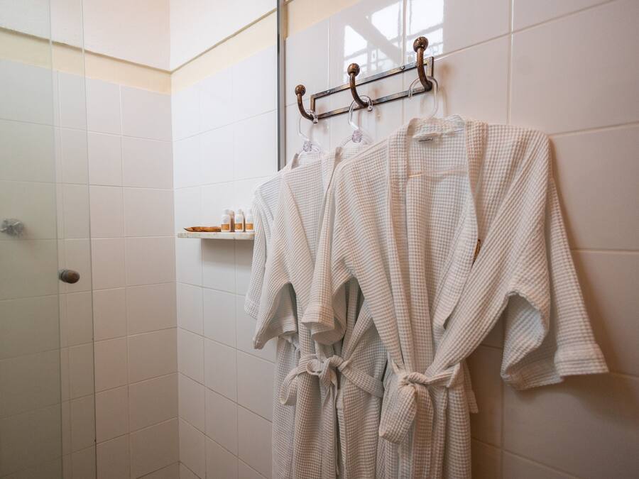 A bathroom with white tiled walls, a shower area, and a towel rack with two towels.