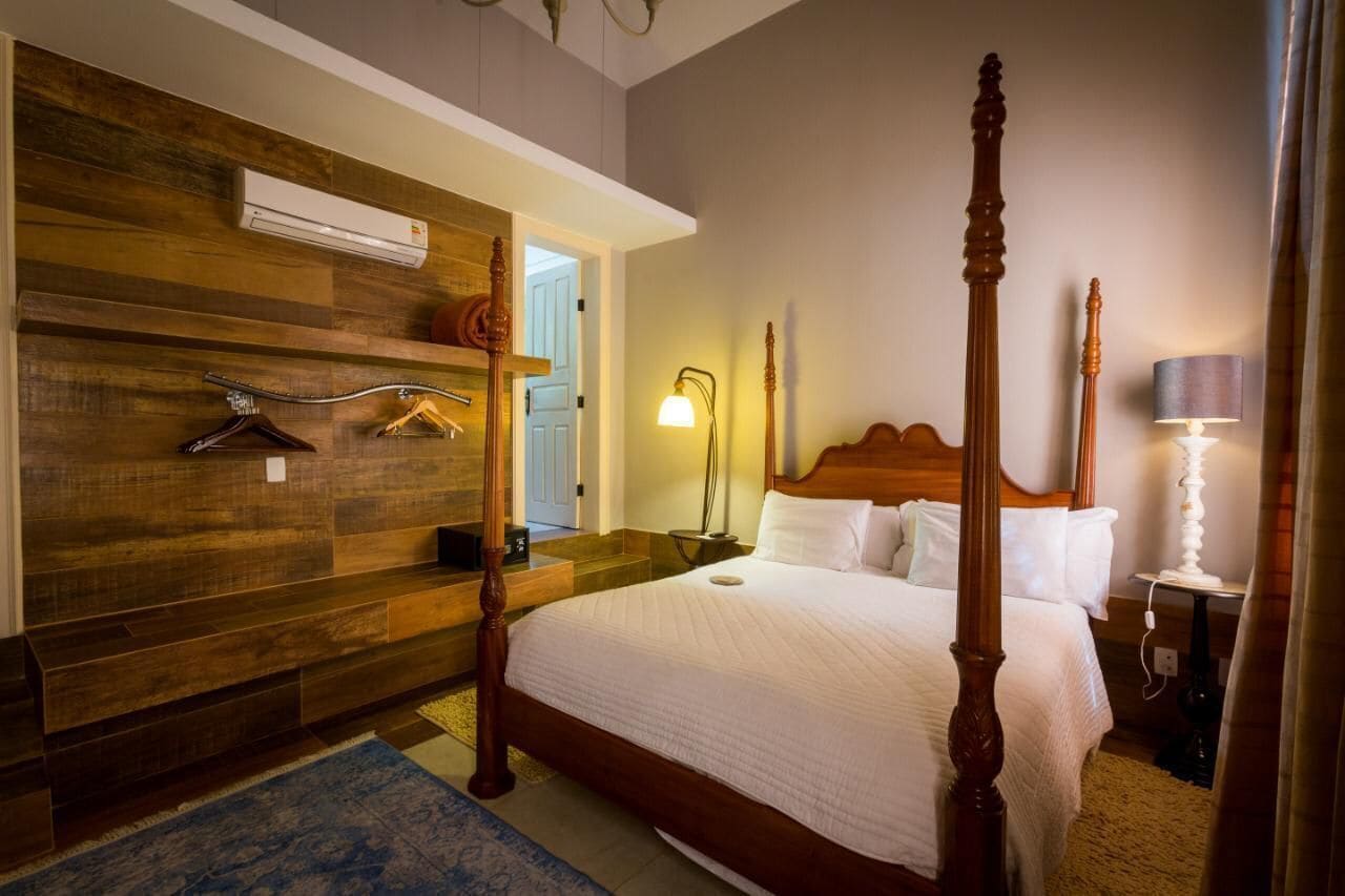 A four-poster bed with a wooden headboard, a wooden wardrobe with a mirror, and a bedside table with a lamp.