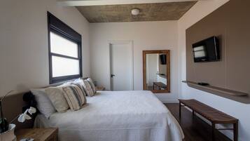 Une chambre à coucher avec un grand lit, un banc en bois, une télévision et un miroir au mur.