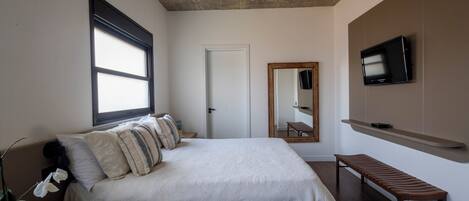 A bedroom with a large bed, a wooden bench, a television, and a mirror on the wall.