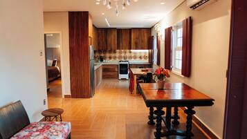 A modern kitchen with wooden cabinets, a dining area with a table and chairs, and a chandelier.