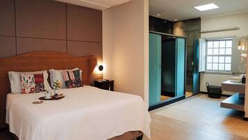 Quarto de hotel moderno com uma cama grande, uma mesa de cabeceira, um espelho, uma janela e uma porta para um banheiro.