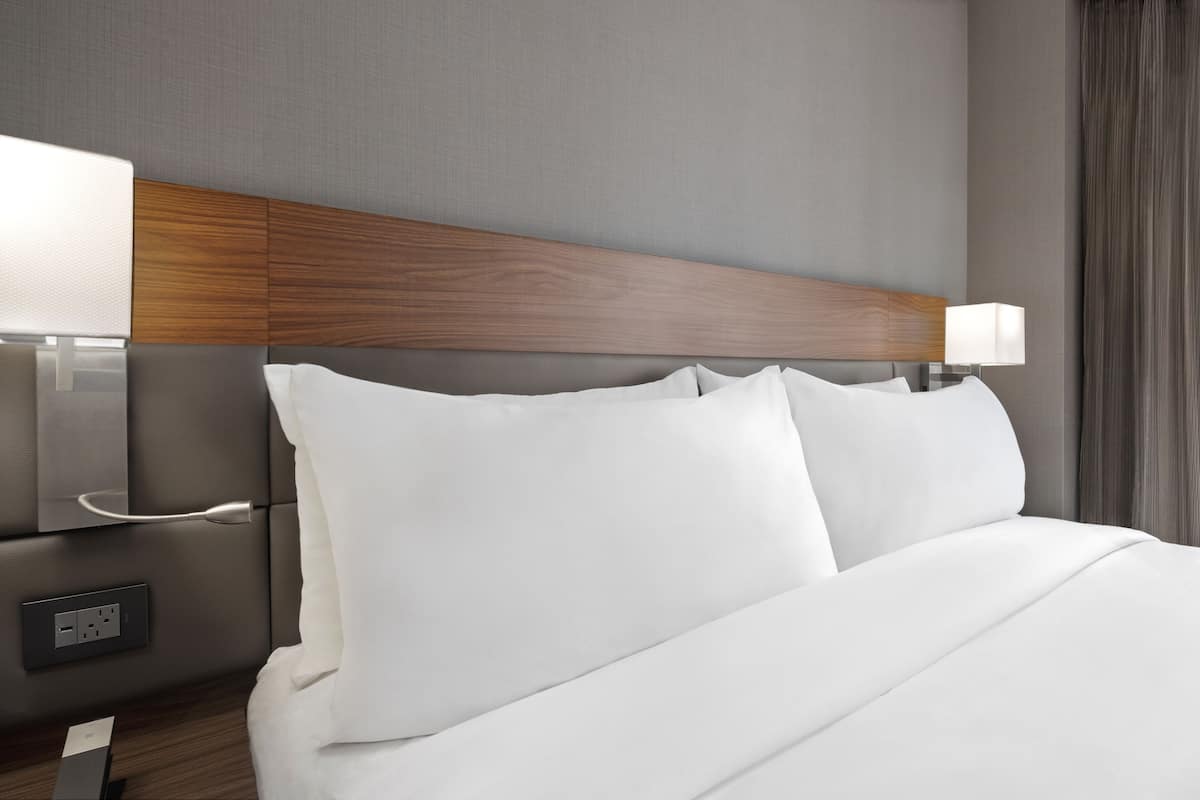 Una habitación de hotel con una cama bien hecha, un cabecero de madera, lámparas de noche y un enchufe.