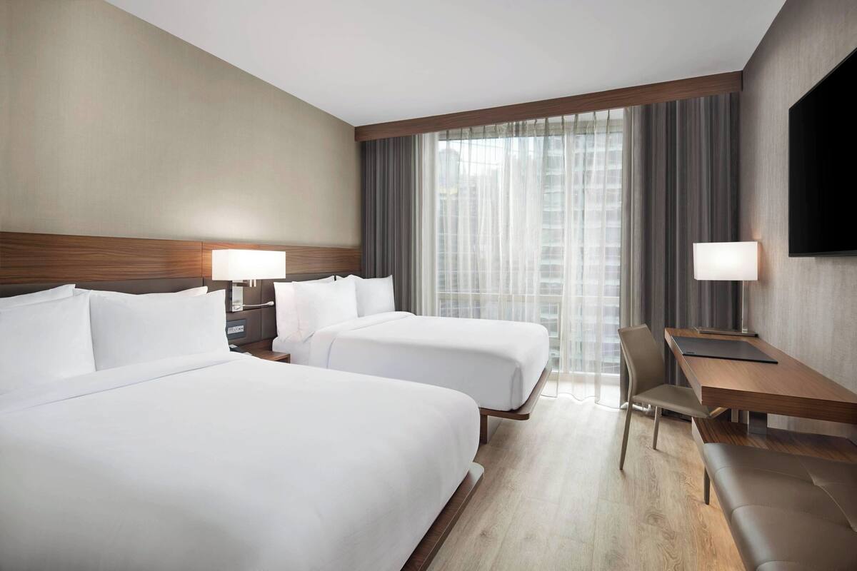 Habitación de hotel con dos camas, un escritorio, una silla, un televisor y una ventana con cortinas.