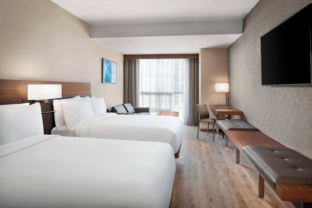 Habitación de hotel con dos camas, un escritorio, una silla, un televisor y una ventana con cortinas.
