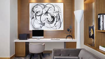 A modern office space with a large abstract painting on the wall, a desk with a computer, a chair, and a sofa.