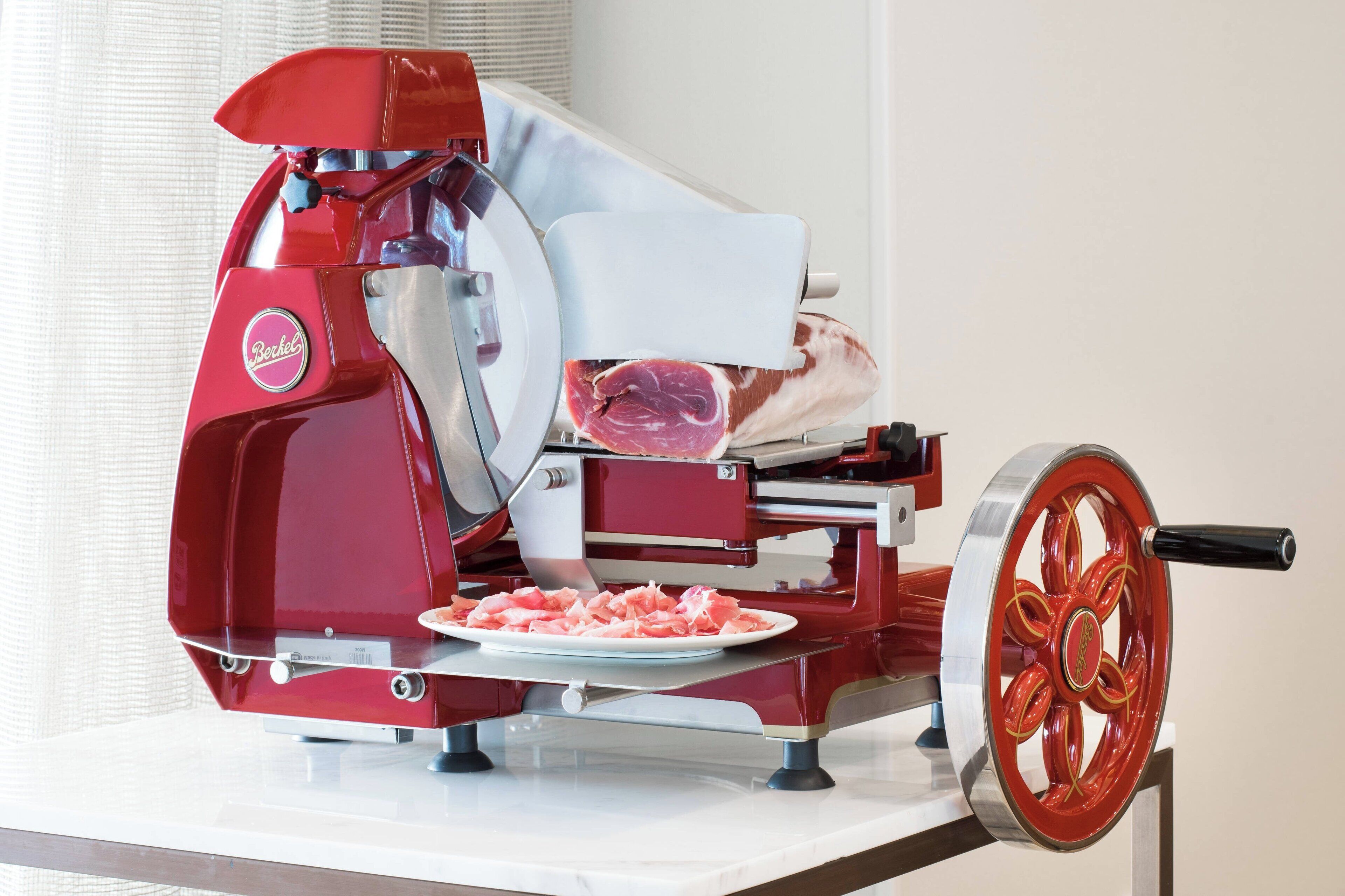 A red meat slicer with a plate of sliced meat and a wheel.