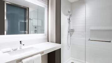 Un baño moderno con un espejo grande, un lavamanos blanco y una zona de ducha con mampara de cristal.