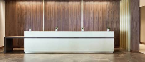 A reception desk with a modern design, flanked by wooden paneling and potted plants.