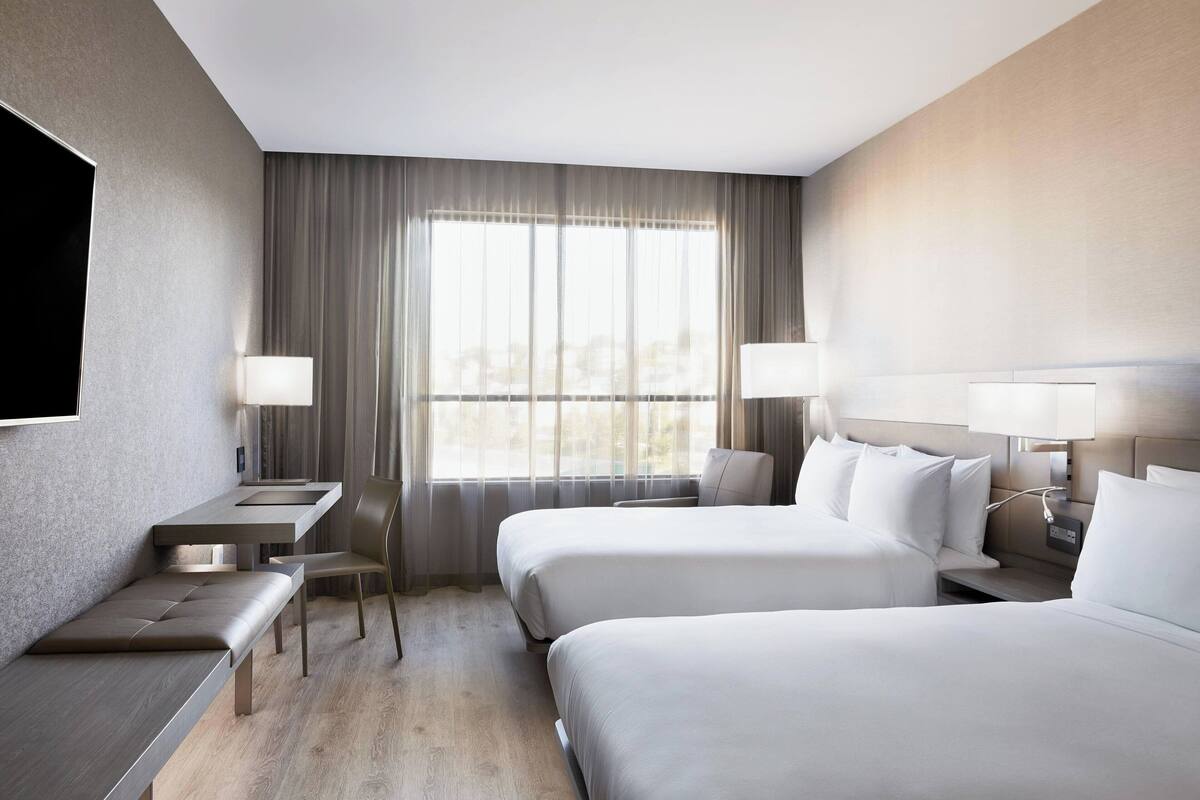 A hotel room with two beds, a desk, a chair, and a TV.