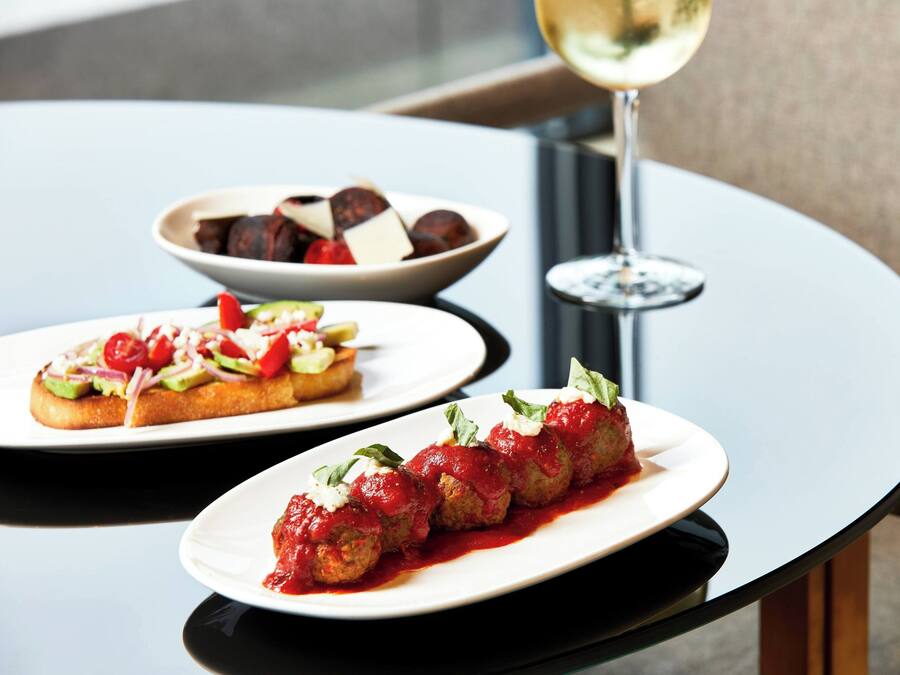 A table with two plates of food, one with meatballs in tomato sauce and another with a salad. A glass of white wine is also visible.
