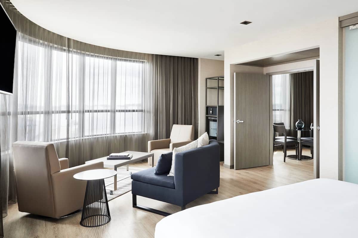 A modern hotel room with a large bed, a sofa, a chair, a small table, and a TV.