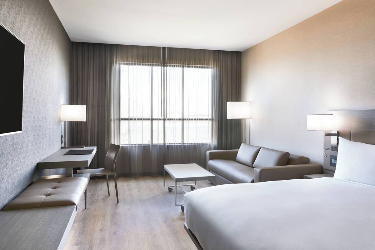 A modern hotel room with a large bed, a sofa, a desk, and a chair.