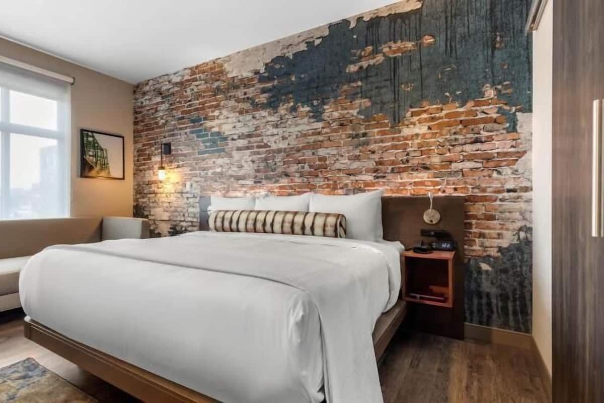 Ein Schlafzimmer mit Ziegelwand, einem Bett, einem Nachttisch, einer Lampe und einem Fenster.