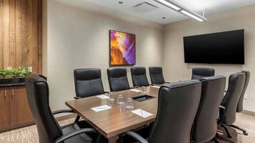 A conference room with a wooden table, black chairs, a flat-screen TV, and a colorful abstract painting on the wall.