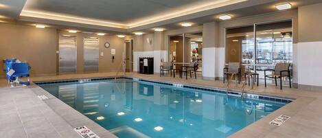 Una piscina interior con agua cristalina, suelo de baldosas y una zona de estar con sillas y mesas.